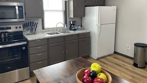Una cocina moderna con electrodomésticos de acero inoxidable, encimera de granito y una mesa de madera con un tazón de manzanas.