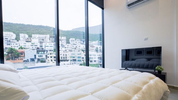 Une chambre dotée d’un grand lit, d’une télévision et offrant une vue sur le paysage urbain grâce à de grandes fenêtres.