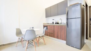 Une cuisine moderne avec un réfrigérateur en acier inoxydable, des armoires en bois et un coin repas comprenant une table blanche et des chaises grises.