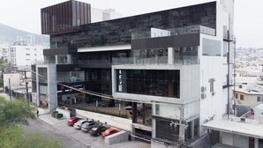 Un bâtiment moderne avec une façade en verre, un parking où sont garées plusieurs voitures et une enseigne de restaurant bien visible.