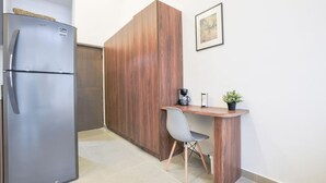 Une petite cuisine équipée comprenant un réfrigérateur en acier inoxydable, un meuble en bois, un petit bureau en bois avec une chaise, une machine à café et une plante en pot.