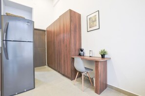 A compact kitchenette with a stainless steel refrigerator, a wooden cabinet, a small wooden desk with a chair, a coffee maker, and a potted plant. - ¡Moderno Loft en San Jerónimo! Cama King + Wifi (Monterrey)
