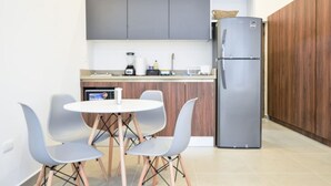 Une cuisine compacte équipée d’un réfrigérateur, d’une machine à café et d’un petit coin repas avec deux chaises et une table.