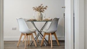 Uma área de refeições com uma mesa posta para dois, apresentando um vaso com plantas secas, duas taças de vinho e um pequeno prato.