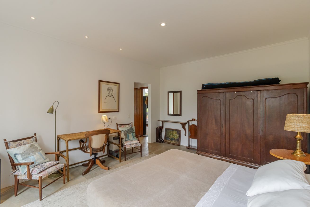 A bedroom with a bed, a wooden wardrobe, a desk with a chair, a lamp, and a framed picture on the wall.