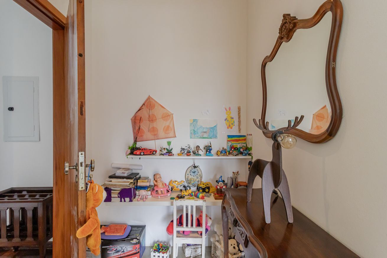 A child's room with a wooden door, a mirror, shelves with toys, and a crib.
