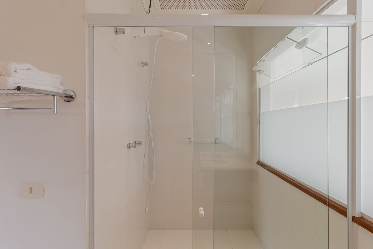 A modern bathroom with a glass shower enclosure, a towel rack with folded towels, and a visible electrical outlet on the wall.