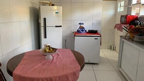 A compact kitchen with a refrigerator, a microwave, and a small countertop. A table with a checkered tablecloth is placed in the center. - Spacious and airy house in Japaratinga, pets allowed. (Japaratinga)