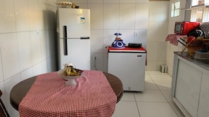 A compact kitchen with a refrigerator, a microwave, and a small countertop. A table with a checkered tablecloth is placed in the center.