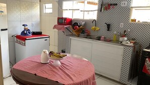 A compact kitchen with a refrigerator, microwave, and sink. A table with a checkered tablecloth and a bowl of fruit is in the center. - Spacious and airy house in Japaratinga, pets allowed. (Japaratinga)