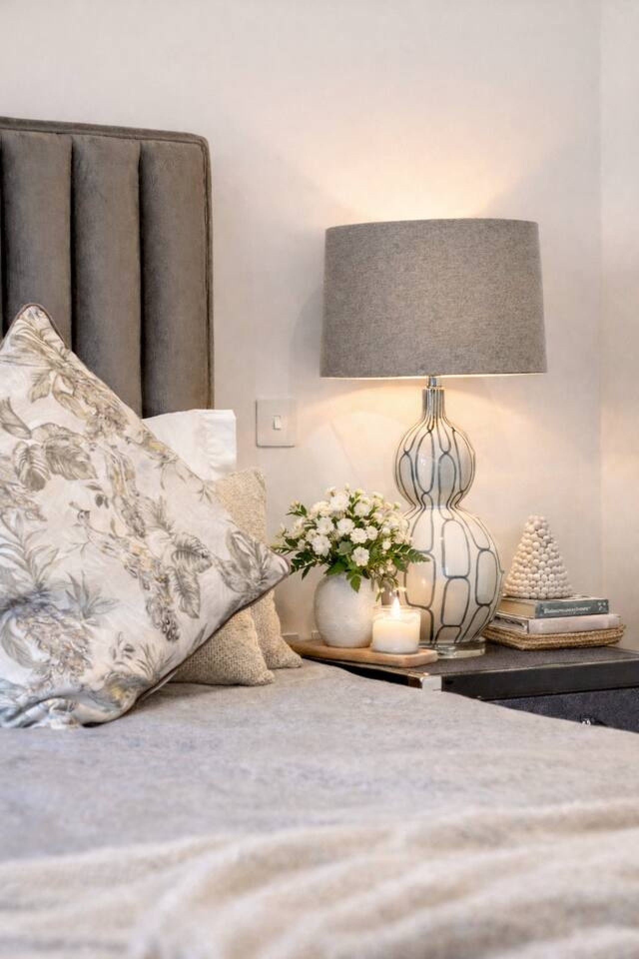 A neatly arranged bedroom with a bed, a bedside lamp, a vase with flowers, and a small decorative item on the nightstand.