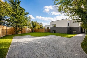 Ein modernes Haus mit gepflasterter Auffahrt, einem eingezäunten Garten und einem gepflegten Rasen.