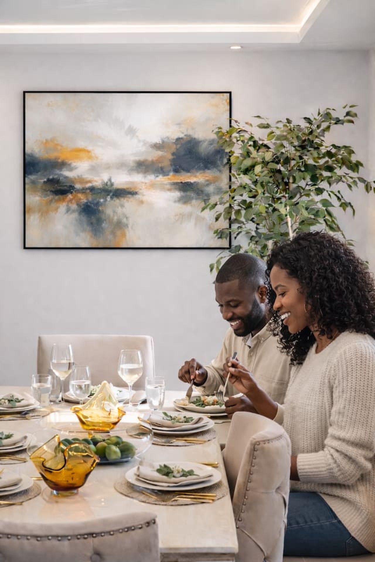 Un comedor con una mesa dispuesta para dos personas, un cuadro en la pared y una planta en maceta.