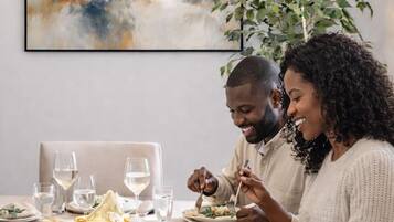 Un comedor con una mesa dispuesta para dos personas, un cuadro en la pared y una planta en maceta.
