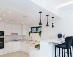 A modern kitchen with white cabinetry, a central island, and pendant lighting. - Luxury 4BR Getaway • Garden • Smart Features (Buckinghamshire)