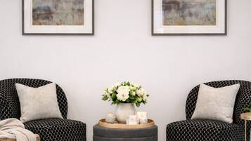 Een kamer met twee zwarte, gestreepte stoelen, een rond poefje, een rieten bijzettafeltje en een vaas met bloemen.