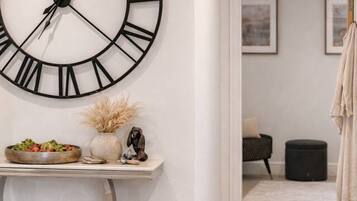 A hallway with a large wall clock, a console table with decorative items, a wicker basket, a brown handbag, and a pair of white sneakers.