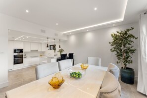 A modern kitchen with white cabinets and a dining area with a table set for four. - Luxury 4BR Getaway • Garden • Smart Features (Buckinghamshire)