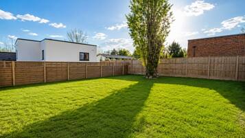 Un jardin avec une pelouse bien entretenue, une clôture en bois et un arbre.