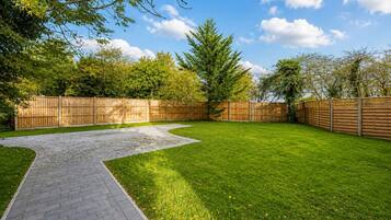 A backyard with a paved pathway, a grassy lawn, and a wooden fence.