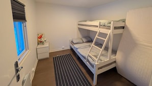 Camera con letto a castello, una finestra, un comodino con un vaso di fiori e un tappeto a righe nere.