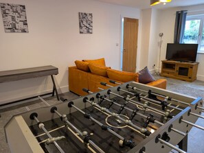 A room with a foosball table, a sofa, and a television. - Family Affair: fun for all in this spacious home (Hanwood)
