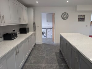 A kitchen with white cabinets, a built-in oven, a toaster, and a washing machine in the background. - Family Affair: fun for all in this spacious home (Hanwood)