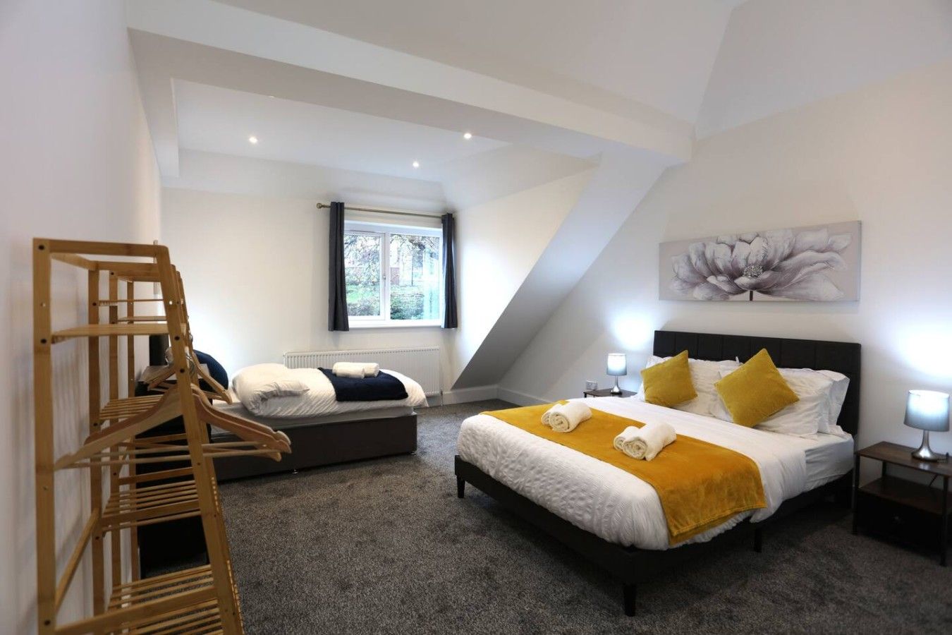 A bedroom with a large bed, a smaller bed, a wooden chair, a window, and a painting on the wall.