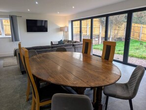 A dining area with a round wooden table, six chairs, a sofa, a TV, and a sliding glass door leading to a backyard. - Family Affair: fun for all in this spacious home (Hanwood)