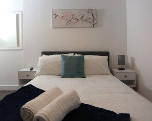 A hotel room with a bed, two bedside tables, a nightstand, a lamp, a painting, and a window. - Contractor House, 4 Bed Ensuite, Near Stadium (West Midlands)