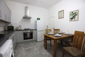 A compact kitchen with a stove, oven, microwave, and refrigerator. There is a dining table with chairs and a small window. - Contractor House, 4 Bed Ensuite, Near Stadium (West Midlands)