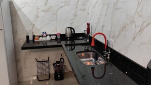 A modern kitchen with marble walls, a black countertop, stainless steel sink, and a red faucet. - Cozy house in Guarujá, 3km from the beach. Air conditioning/Wi-Fi/barbecue. (Guarujá)