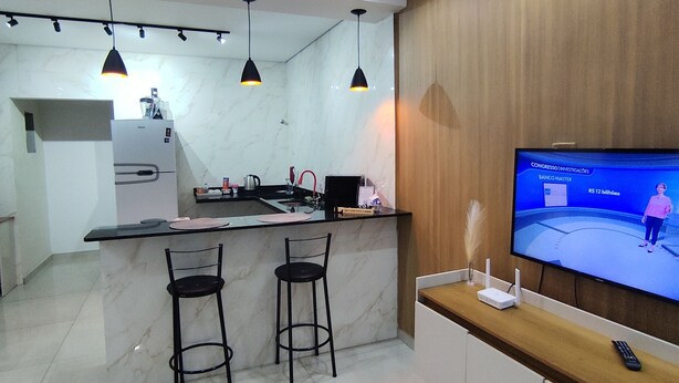A modern kitchen with a marble countertop, two bar stools, a built-in oven, and a wooden accent wall. - Cozy house in Guarujá, 3km from the beach. Air conditioning/Wi-Fi/barbecue. (Guarujá)