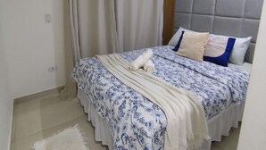 A bedroom with a bed, a white rug, a grey padded headboard, and a window with curtains. - Cozy house in Guarujá, 3km from the beach. Air conditioning/Wi-Fi/barbecue. (Guarujá)