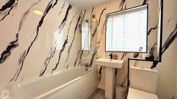 Une salle de bain avec un mur en marbre, une baignoire, un lavabo et des toilettes.