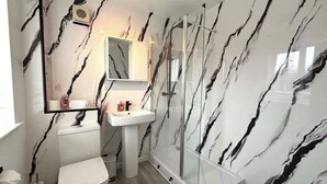 Un bagno con una parete in marmo bianco, un lavabo bianco, un water e un box doccia in vetro.