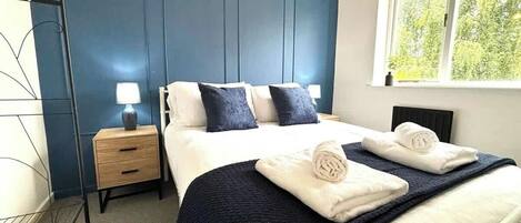Une chambre d’hôtel avec un lit, des tables de chevet et une fenêtre donnant sur un paysage verdoyant.