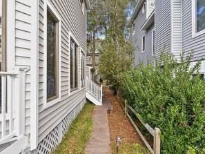 A narrow pathway flanked by white houses with a wooden fence and greenery. - Coastal House Near the Beach | Kitchen, Deck & BBQ (Bethany Beach)