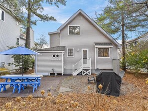 A two-story house with a covered patio, a small deck, and a barbecue grill. - Coastal House Near the Beach | Kitchen, Deck & BBQ (Bethany Beach)