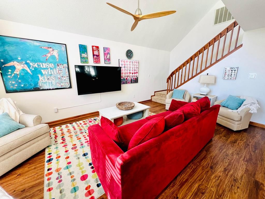 A living room with a red sofa, a television, a ceiling fan, and a staircase.