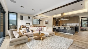 A modern living room with a sectional sofa, a round coffee table, and a kitchen area with a bar and high chairs. - Hot Tub with Slope Views | Walk to Lift (Park City)
