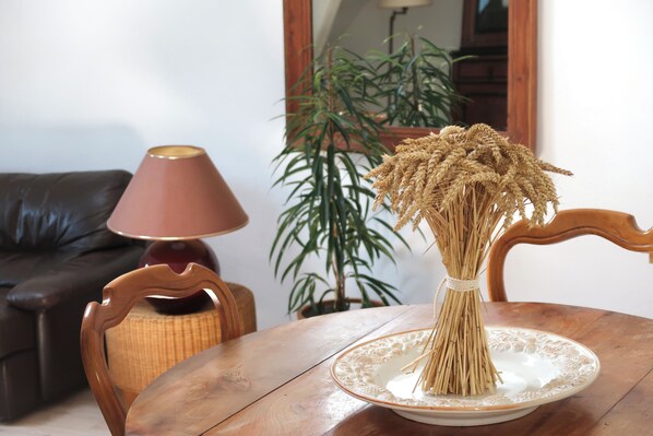 A wooden table with a plate holding a bunch of wheat stalks, a brown leather couch, a lamp, and a potted plant in the background. - La grange à grains (Château-Renard)