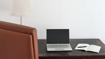 Ein Laptop auf einem Nachttisch aus Holz, neben ihm ein Buch und ein Stift.