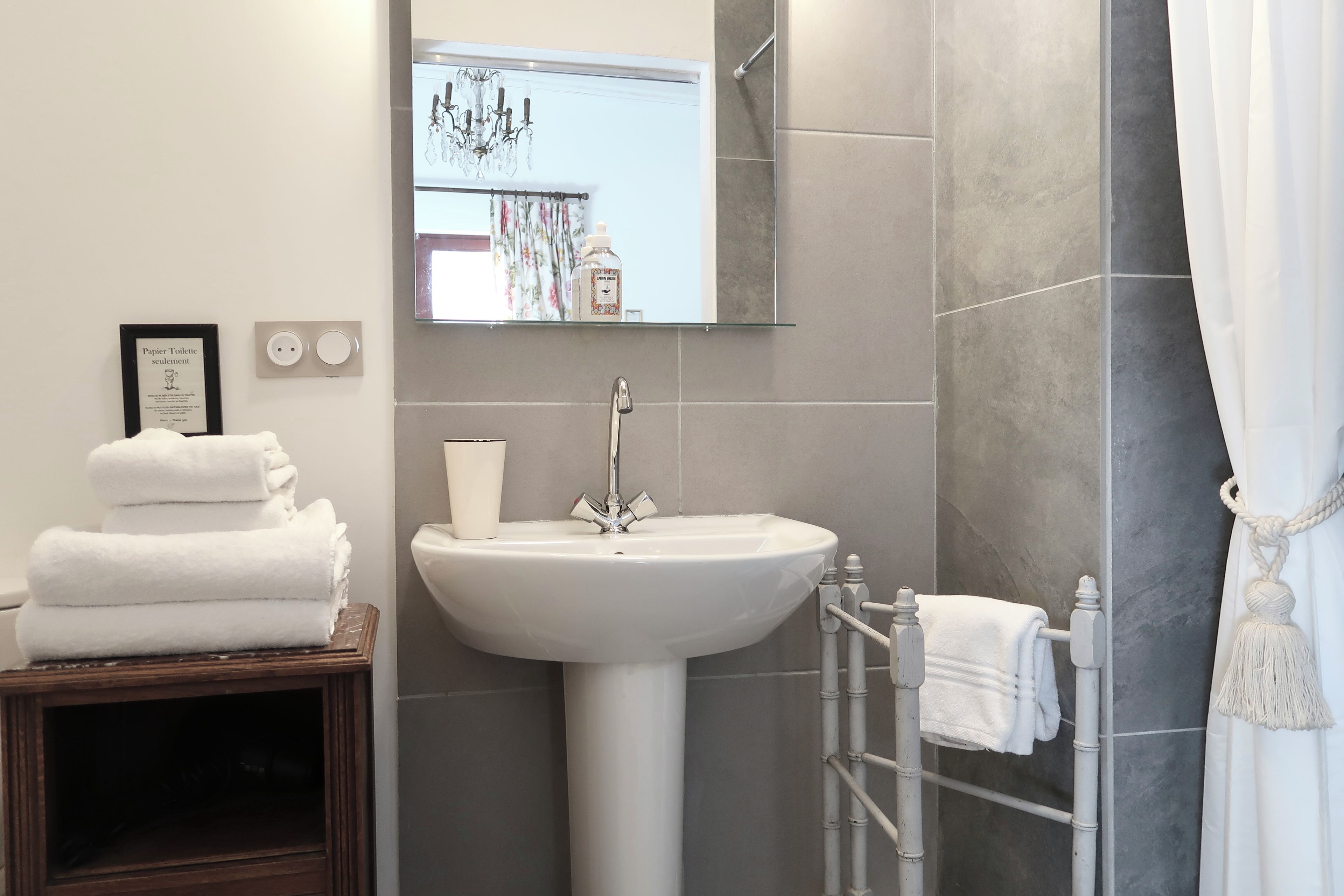 A bathroom with a white sink, a mirror, a towel rack, and a framed sign on the wall.