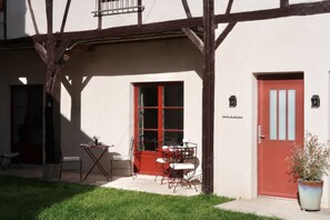 Un immeuble avec une porte rouge, un balcon et un petit espace extérieur aménagé avec des tables et des chaises.