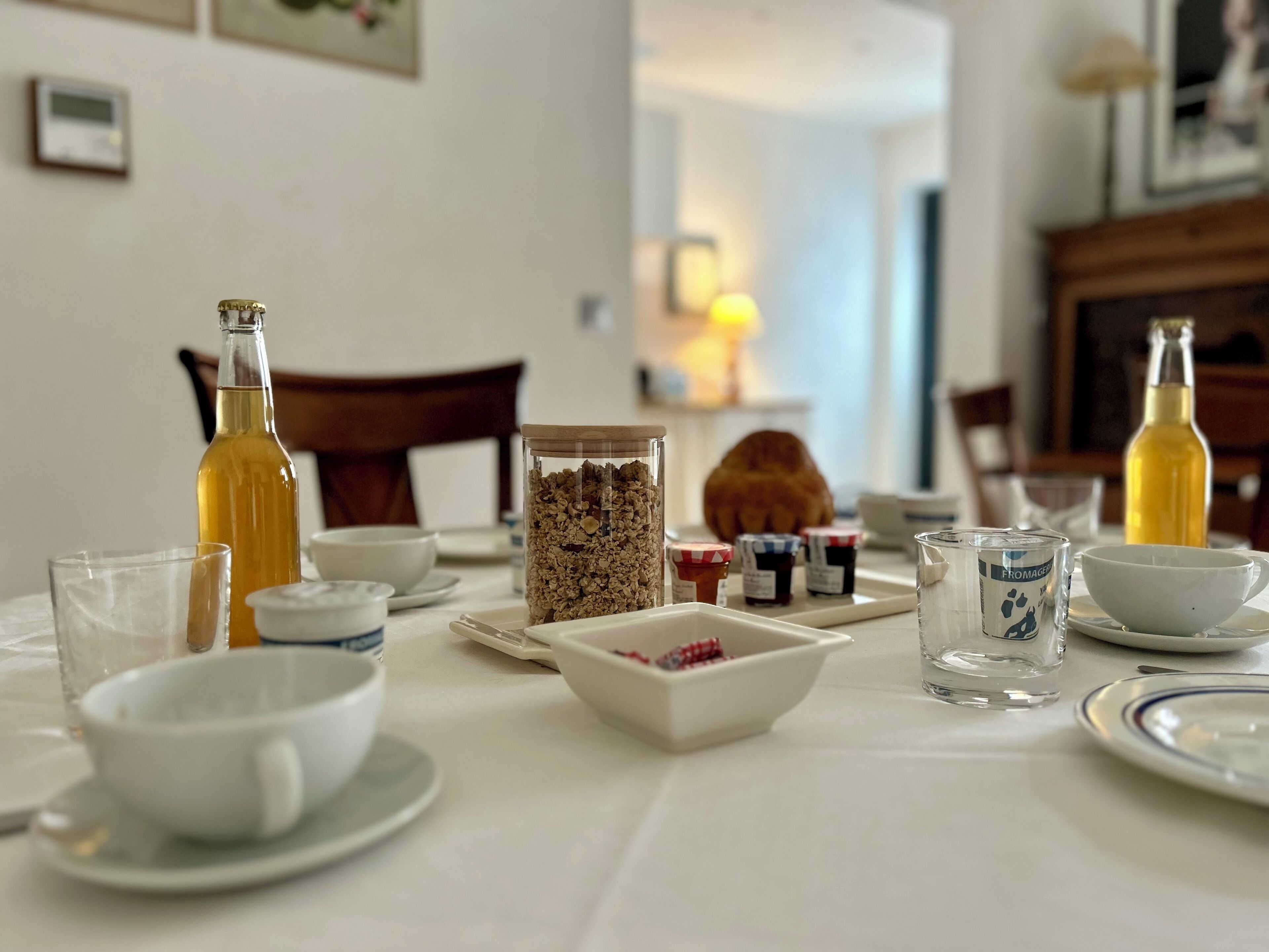 Ontbijttafel gedekt met verschillende soorten eten, waaronder een fles, een pot granola en meerdere kleine bakjes met spreads.