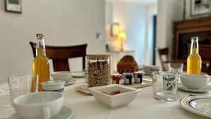 A breakfast table set with various food items, including a bottle, a jar of granola, and several small containers of spreads. - La grange à grains (Château-Renard)