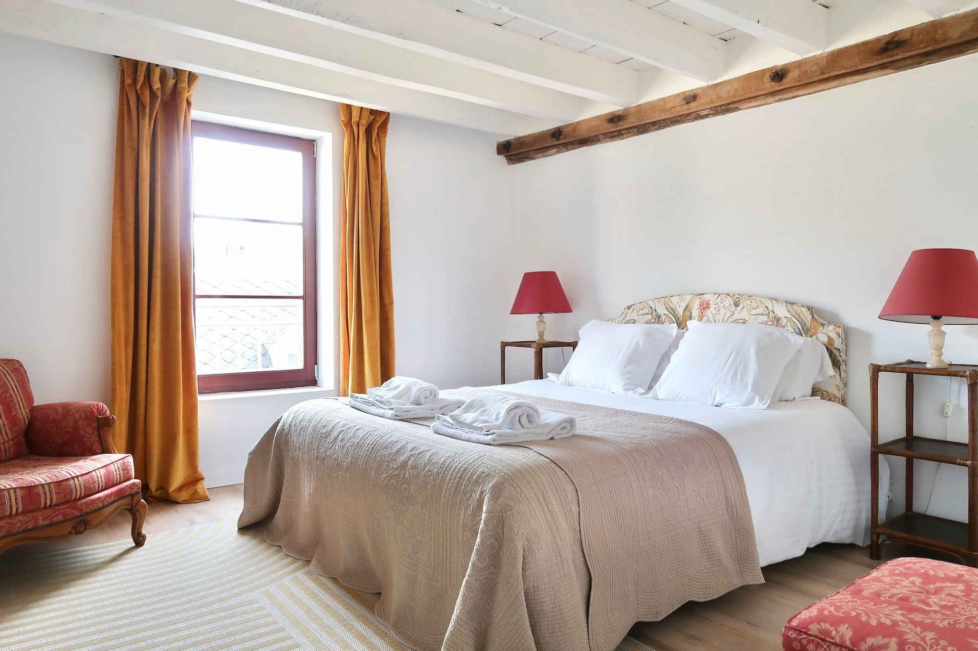 Een slaapkamer met een bed, twee nachtkastjes met lampen, een stoel en een raam met gordijnen.