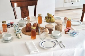 Une table mise pour le petit-déjeuner, avec une nappe, de l’argenterie, des assiettes, des tasses, une variété d’aliments et des condiments.
