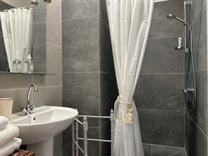Casa de banho com uma pia branca, espelho e chuveiro.
